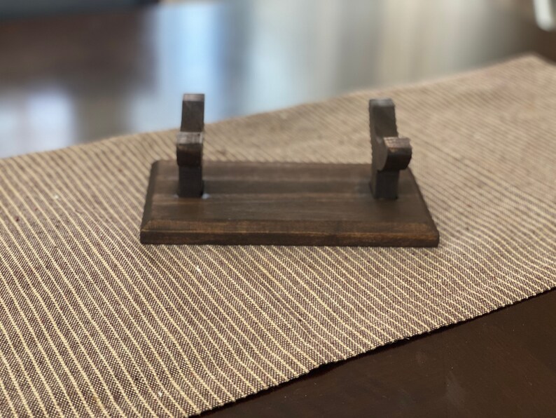 May include: A wooden stand with two upright arms for holding a sword or other long object. The stand is dark brown and has a smooth finish.