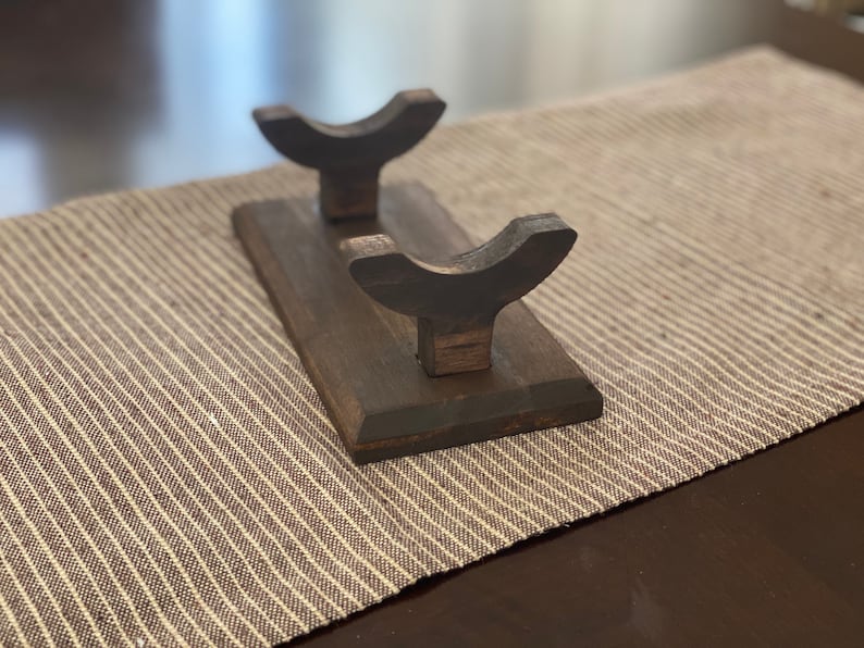 May include: A wooden stand with two curved arms for holding swords or other long objects. The stand is dark brown and has a smooth finish.