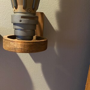 Pu&ograve; includere: Un supporto a parete in legno con un oggetto in metallo grigio e marrone attaccato. Il supporto ha una base circolare e un pezzo laterale rettangolare.