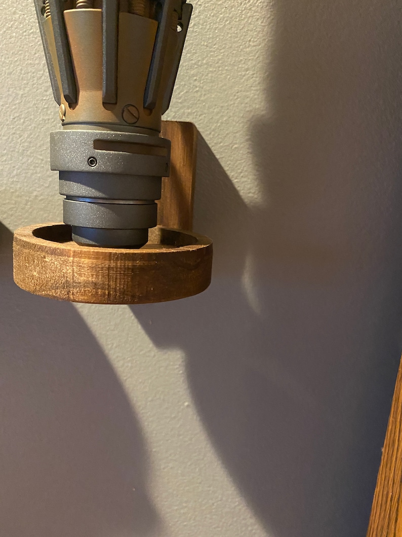 Pu&ograve; includere: Un supporto a parete in legno con un oggetto in metallo grigio e marrone attaccato. Il supporto ha una base circolare e un pezzo laterale rettangolare.