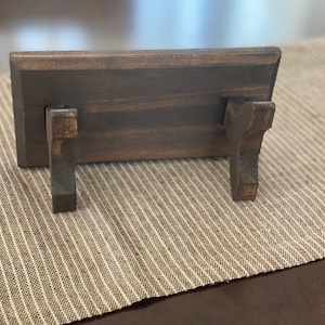 Puede incluir: Un estante de madera marr&oacute;n oscuro con dos peque&ntilde;os soportes de madera marr&oacute;n oscuro en la parte inferior. El estante est&aacute; sobre una superficie de rayas marrones y blancas.