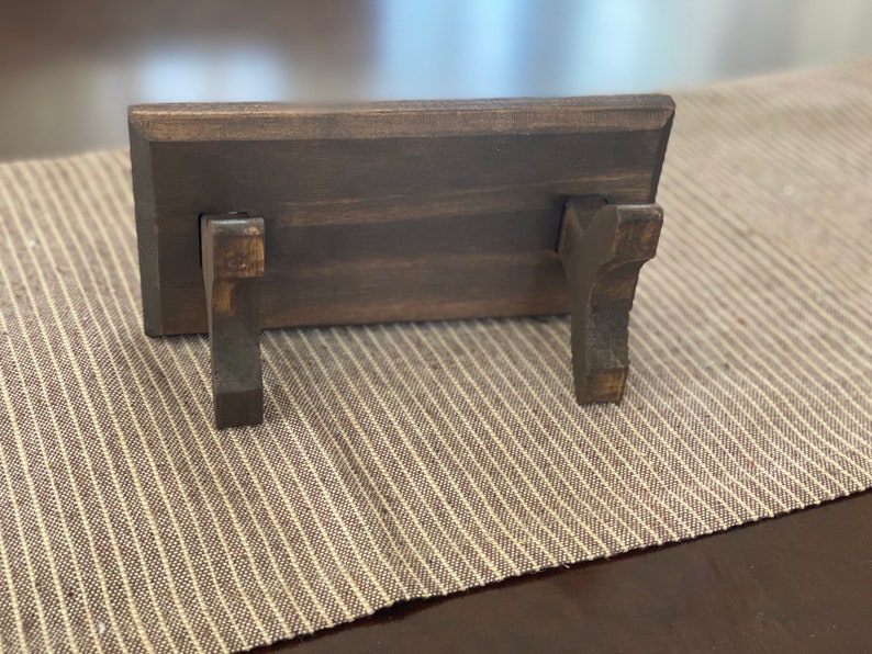 Puede incluir: Un estante de madera marr&oacute;n oscuro con dos peque&ntilde;os soportes de madera marr&oacute;n oscuro en la parte inferior. El estante est&aacute; sobre una superficie de rayas marrones y blancas.