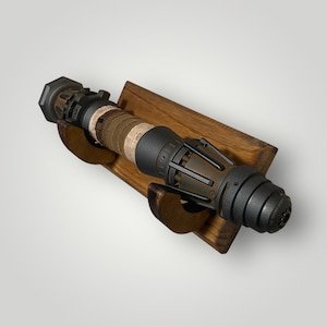 May include: A dark gray and brown lightsaber with a wooden wall mount. The lightsaber has a weathered, distressed look and features a metal casing with a brown leather wrap.