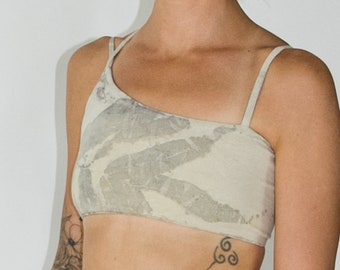 Puede incluir: Un top blanco corto con un estampado de hojas y tirantes finos. El top está hecho de una tela suave y ligera. La modelo lleva una falda a juego con un estampado de hojas similar.