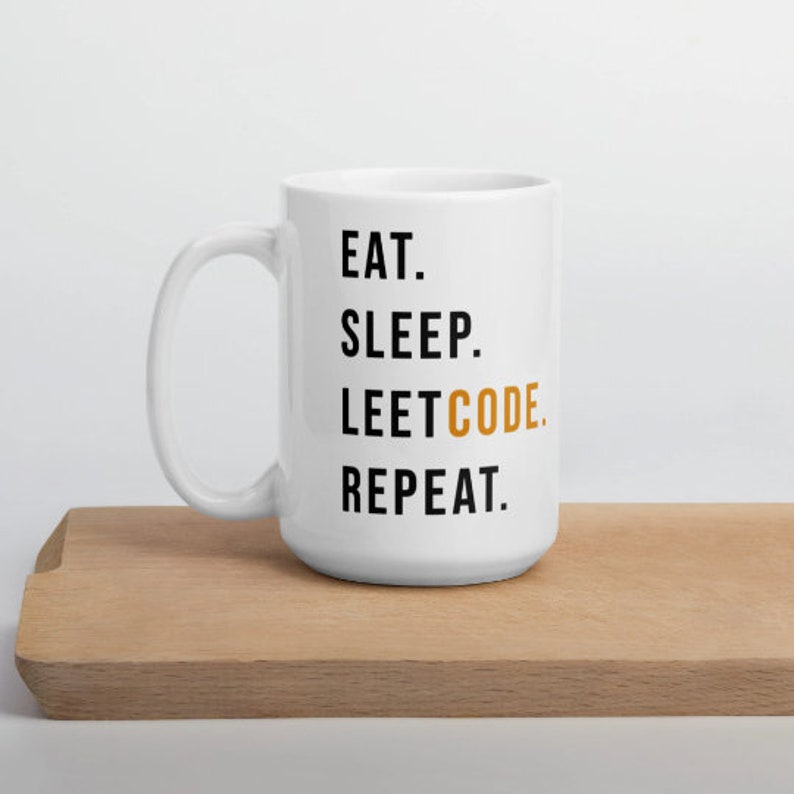 May include: White ceramic mug with the text "EAT. SLEEP. LEETCODE. REPEAT." in black and orange lettering. The mug is on a light brown wooden cutting board.