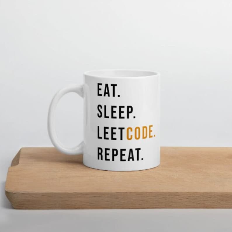 May include: White ceramic mug with the words "EAT. SLEEP. LEETCODE. REPEAT." printed in black and gold. The mug is on a wooden surface.