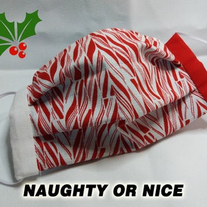May include: A white and red striped face mask with a white border and red trim. The mask has a white elastic band. The text "NAUGHTY OR NICE" is printed below the mask.