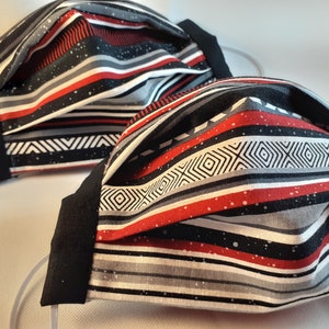 May include: Two black and white striped face masks with red stripes and white speckles. The masks are pleated and have black elastic ear loops.