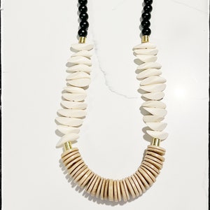 May include: A long necklace with black, white, and brown wooden beads. The necklace has a gold clasp.
