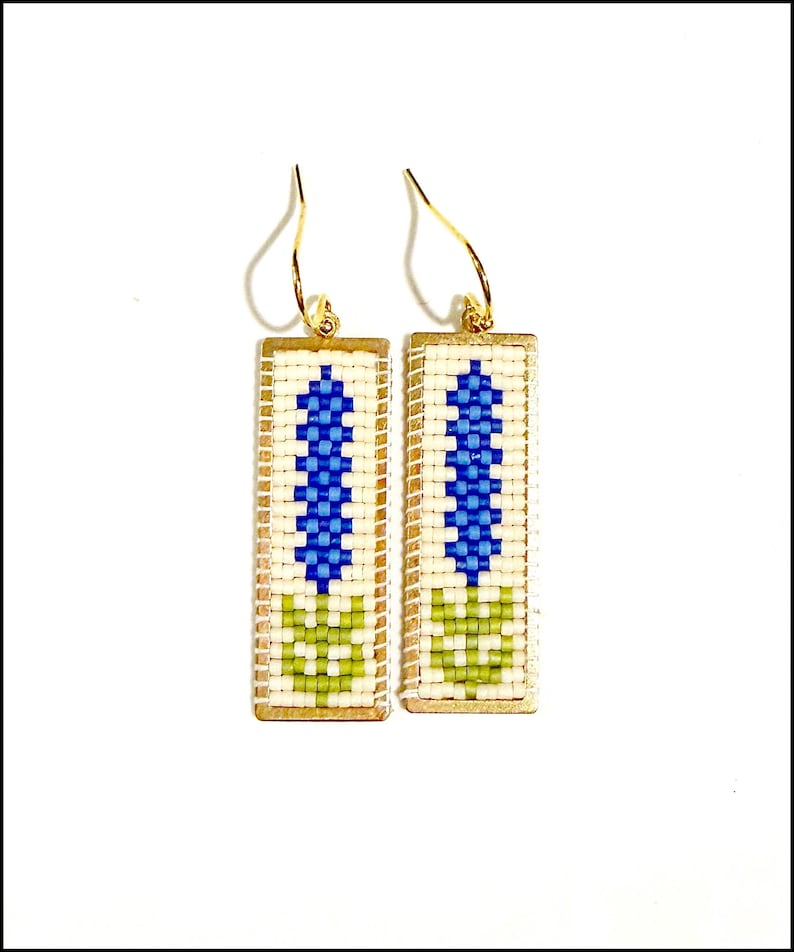 May include: A pair of rectangular earrings with gold-colored hooks. Each earring features a cream-colored background with a blue and green floral design. The earrings are made with small beads.