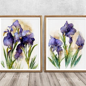 May include: Two framed watercolor prints featuring vibrant purple iris flowers with green stems and leaves. The artwork has a soft, painterly style, set against a neutral background. The frames are a warm, natural wood tone, adding to the artwork's aesthetic.