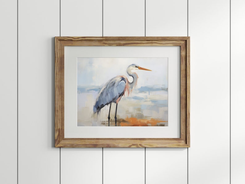 Puede incluir: Una pintura enmarcada de una garza azul de pie en una playa con un fondo borroso de agua y cielo.