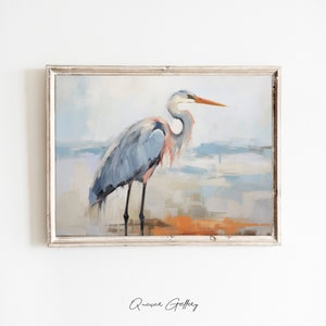 Puede incluir: Una pintura de una garza azul de pie en una playa con un fondo azul claro y blanco. La garza tiene un pico largo y delgado y patas largas. La pintura est&aacute; enmarcada en un marco blanco.