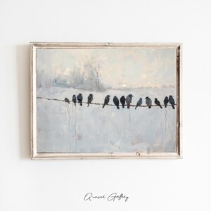 May include: A framed painting depicts a winter scene with a row of black birds perched on a wire against a pale blue and white background. The artwork has a vintage aesthetic, with a silver-colored frame and a soft, painterly style.
