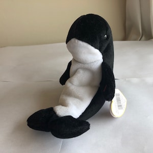 Puede incluir: Juguete de peluche negro y blanco con forma de orca. El juguete tiene la barriga blanca y la espalda y las aletas negras.