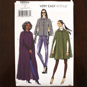May include: Vogue V8959 sewing pattern featuring cape designs. The pattern includes illustrations of capes in various styles, including a purple full-length cape, a black and white checkered cape, and a green cape. The pattern is for sizes Lrg-XXL.
