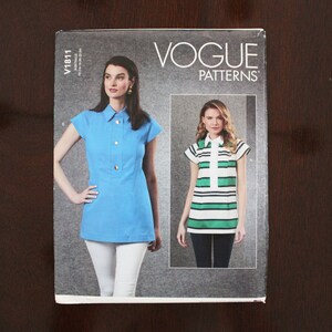 May include: Vogue Patterns sewing pattern, V1811, for a tunic top with short sleeves. The pattern shows two models wearing the tunic top in different colors and patterns. One model is wearing a solid blue tunic top with white pants, and the other model is wearing a striped green and white tunic top with black pants.