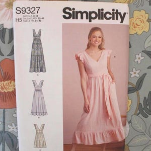 May include: A Simplicity S9327 sewing pattern envelope for a V-neck dress with flutter sleeves and a ruffled hem. The front shows three line-art variations labeled A, B, and C, and a photograph of a light pink dress in U.S. sizes 6-14.