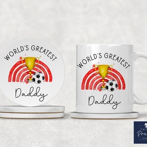Puede incluir: Taza de cer&aacute;mica blanca con un arco&iacute;ris rojo y blanco, un trofeo dorado y un bal&oacute;n de f&uacute;tbol. El texto "World's Greatest Daddy" est&aacute; impreso en la taza.