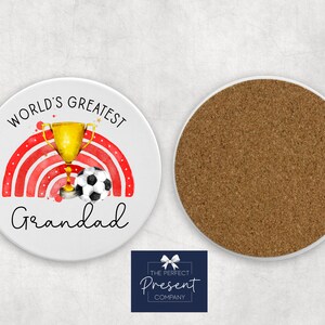 Puede incluir: Posavasos redondo blanco con un dise&ntilde;o de arco&iacute;ris rojo y blanco, un trofeo dorado y un bal&oacute;n de f&uacute;tbol blanco y negro. El texto "World's Greatest Grandad" est&aacute; impreso en el posavasos.