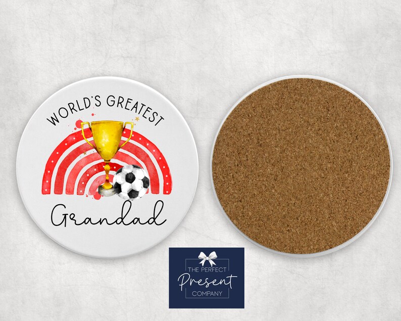 Puede incluir: Posavasos redondo blanco con un dise&ntilde;o de arco&iacute;ris rojo y blanco, un trofeo dorado y un bal&oacute;n de f&uacute;tbol blanco y negro. El texto "World's Greatest Grandad" est&aacute; impreso en el posavasos.