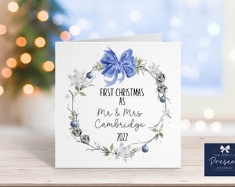 May include: A white Christmas card with a blue and silver wreath design. The text on the card reads "First Christmas as Mr & Mrs Cambridge 2022".
