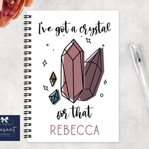 May include: A white spiral bound notebook with a pink and black illustration of crystals and the text "I've got a crystal for that REBECCA".