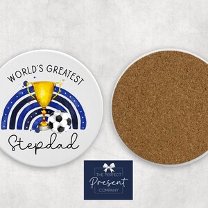 Puede incluir: Posavasos de cer&aacute;mica blanca con un dise&ntilde;o de acuarela azul y dorado. El dise&ntilde;o presenta un trofeo, un bal&oacute;n de f&uacute;tbol y el texto "World's Greatest Stepdad".