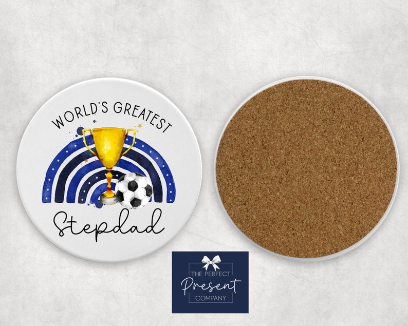 Puede incluir: Posavasos de cer&aacute;mica blanca con un dise&ntilde;o de acuarela azul y dorado. El dise&ntilde;o presenta un trofeo, un bal&oacute;n de f&uacute;tbol y el texto "World's Greatest Stepdad".