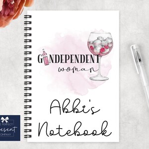 May include: A pink and white watercolor design with a glass of pink gin and a bottle of pink wine. The text "Gindependent woman" is written in black. The notebook is titled "Abbi's Notebook".