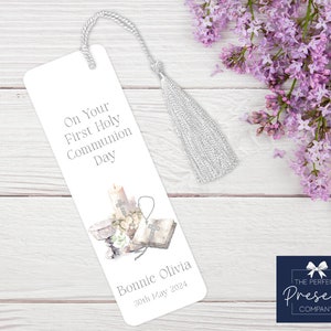 May include: White bookmark with a silver tassel. The bookmark features a watercolor illustration of a candle, chalice, and bible with the text "On Your First Holy Communion Day" and "Bonnie Olivia 30th May 2024".