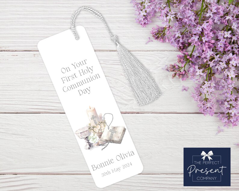 May include: White bookmark with a silver tassel. The bookmark features a watercolor illustration of a candle, chalice, and bible with the text "On Your First Holy Communion Day" and "Bonnie Olivia 30th May 2024".