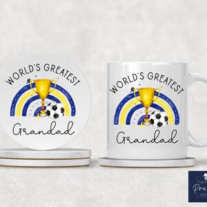Puede incluir: Conjunto de taza y posavasos de cer&aacute;mica blanca con un arco&iacute;ris azul y amarillo, un trofeo dorado y un bal&oacute;n de f&uacute;tbol. El texto "World's Greatest Grandad" est&aacute; impreso en la taza y el posavasos.