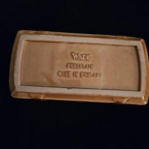 May include: A rectangular, light brown Wade porcelain dish with a raised border. The base features embossed text: "Wade Porcelain Made in England."