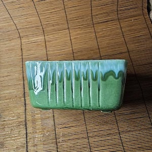 May include: Rectangular ceramic planter with a green and blue glaze. The planter has vertical ridges and a glossy finish. A decorative container for plants, suitable for indoor or outdoor use.