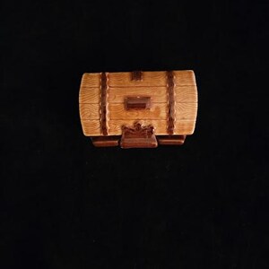 May include: A decorative, barrel-shaped ceramic container with a light brown wood grain finish. Dark brown bands and accents add detail. The container has a small, rectangular door and sits on a dark brown base.