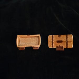 May include: Two miniature wooden barrel-shaped containers. One is open, revealing a wood-grain interior. The other is closed, with a hinged lid and decorative bands. Both are brown and tan.
