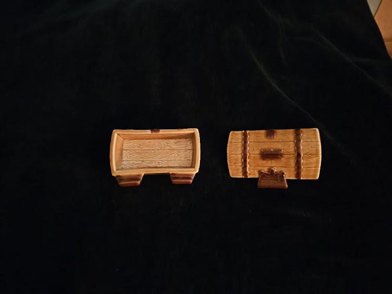 May include: Two miniature wooden barrel-shaped containers. One is open, revealing a wood-grain interior. The other is closed, with a hinged lid and decorative bands. Both are brown and tan.