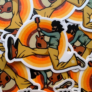 May include: A retro-style sticker featuring a cartoon illustration of a person with an afro, wearing bell-bottom pants and playing a guitar. The person is jumping in the air, and the background is a colorful, concentric circle design.