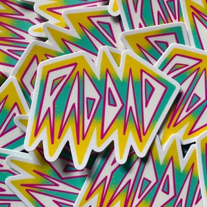 May include: A stack of stickers with a yellow, green, and pink gradient design. The stickers feature the word "RAD" in a bold, white font.