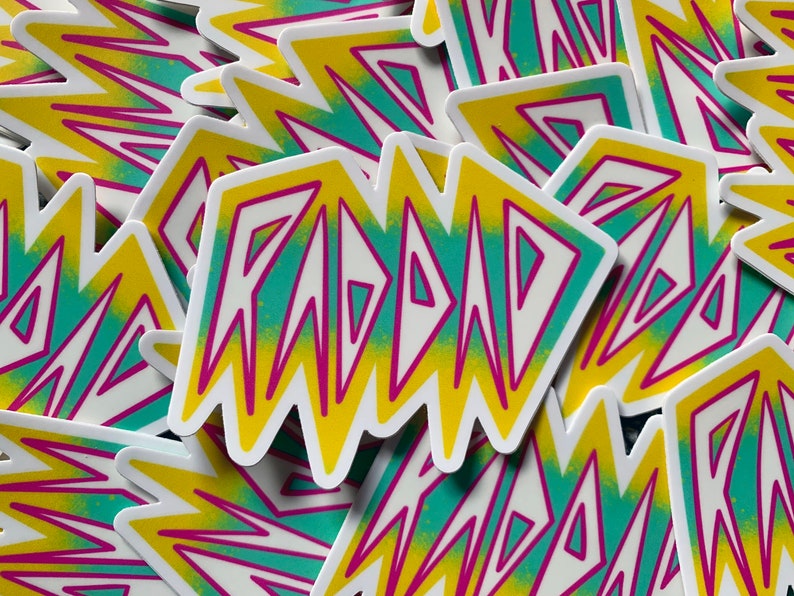 May include: A stack of stickers with a yellow, green, and pink gradient design. The stickers feature the word "RAD" in a bold, white font.