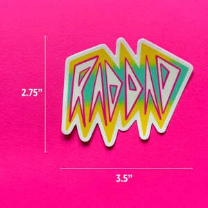 May include: A white sticker with the word "RAD" in yellow, pink, and blue letters. The sticker is 3.5 inches wide and 2.75 inches tall.