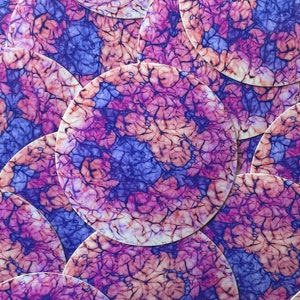 May include: A close-up of a stack of round, colorful coasters with a pink, purple, and blue marbled design.