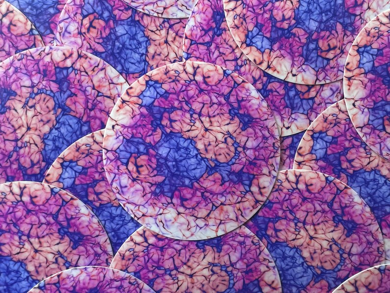 May include: A close-up of a stack of round, colorful coasters with a pink, purple, and blue marbled design.
