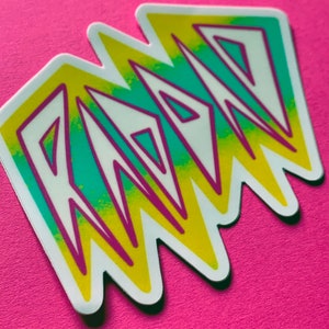 May include: A sticker with the word "RAD" in a stylized font. The letters are outlined in purple and filled with a gradient of yellow and teal.