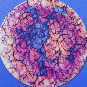 May include: A round, white surface with a marbled pattern in shades of pink, purple, and blue. The marbling resembles veins or cracks in the surface.