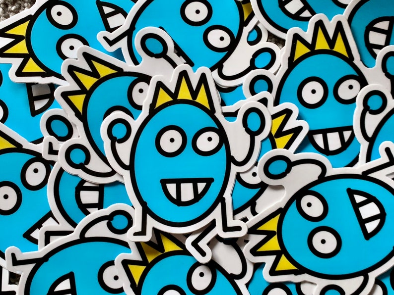 May include: A close-up of several blue and yellow cartoon monster stickers. The stickers have different expressions and features, including a crown, spikes, and teeth.