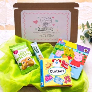 May include: A brown cardboard gift box with a label reading THANK YOU FOR BEING A PART OF OUR SPECIAL DAY TOM & FIONA, containing a green bag of apple soft biscotti, an Organix snack bar, a Peppa Pig book, and a small book titled Clothes.