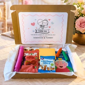 May include: A brown cardboard gift box containing assorted snacks and toys, including Bear fruit yoyos, coconut rolls, and a Peppa Pig activity book. The lid features a printed label with a cartoon bride and groom and the text Thank You For Being A Part Of Our Special Day Shannon & Tommy.