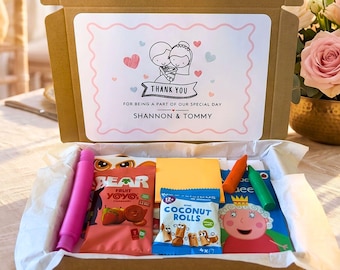 May include: A brown cardboard gift box containing assorted snacks and toys, including Bear fruit yoyos, coconut rolls, and a Peppa Pig activity book. The lid features a printed label with a cartoon bride and groom and the text Thank You For Being A Part Of Our Special Day Shannon & Tommy.
